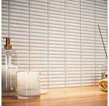 Scène avec des carreaux muraux blancs et allongés, un distributeur de savon, une bougie et une serviette sur une table en bois