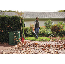 Un homme utilise un souffleur de feuilles dans le jardin, à côté d'un sac à déchets verts et d'un râteau.