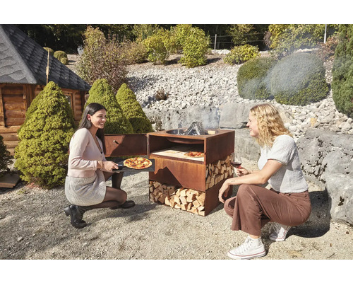 Four à pizza en acier avec du bois et deux femmes dans le jardin.