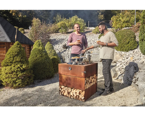 Deux hommes font des grillades sur un barbecue en acier Corten dans le jardin, rempli de bûches.