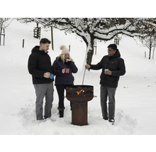 Des personnes se tiennent autour d'un foyer dans la neige, avec des arbres en arrière-plan.