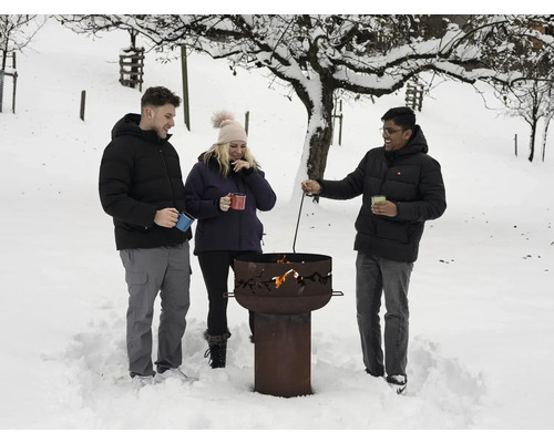 Des personnes se tiennent autour d'un foyer dans la neige, avec des arbres en arrière-plan.
