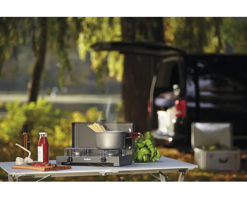 Réchaud de camping avec casserole, ingrédients et voiture en arrière-plan