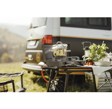 Cuisine de camping avec réchaud à gaz, casserole, lanterne et aliments devant un camping-car
