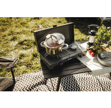 Scène de camping avec réchaud, casserole et accessoires sur une table à l'extérieur.