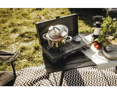 Scène de camping avec réchaud, casserole et accessoires sur une table à l'extérieur.