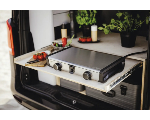 Cuisine de camping avec plaque de cuisson, herbes aromatiques, tomates et planche à découper dans le coffre d'une voiture.
