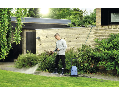 Un homme nettoie un trottoir dans le jardin avec un nettoyeur haute pression.