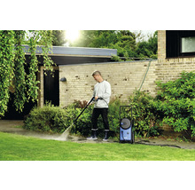 Un homme nettoie une allée de jardin avec un nettoyeur haute pression.
