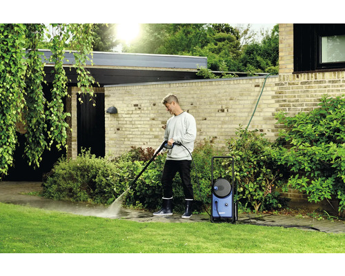 Un homme nettoie une allée de jardin avec un nettoyeur haute pression.