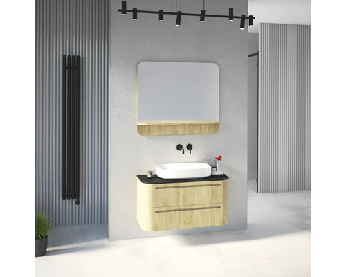Salle de bains avec meuble en bois clair, vasque blanche, robinetterie murale noire, miroir avec étagère et radiateur vertical noir.