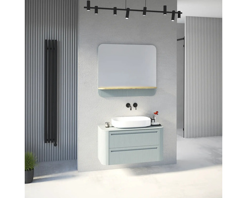 Salle de bain moderne avec meuble sous-vasque nervuré vert clair, vasque à poser blanche, robinetterie murale noire et miroir avec étagère.