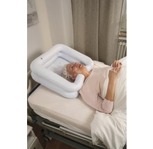 Eine ältere Frau liegt in einem Bett mit einem aufblasbaren Haarwaschbecken um ihren Kopf.