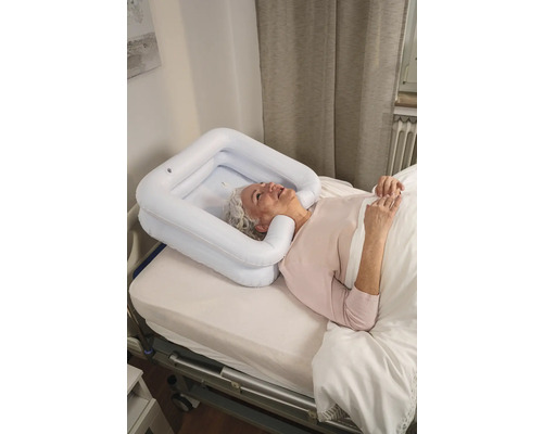 Eine ältere Frau liegt in einem Bett mit einem aufblasbaren Haarwaschbecken um ihren Kopf.
