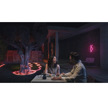 Szene einer abendlichen Gartenparty mit beleuchtetem Baum und Paar beim Abendessen im Freien