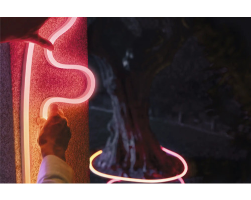 Person befestigt LED-Neonflexband an einer Wand und an einem Baum.