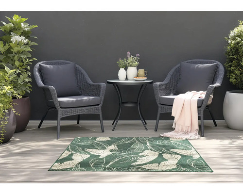 Scène de jardin avec deux fauteuils en rotin, une petite table et un tapis vert à motif de feuilles