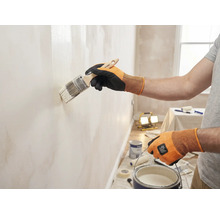 Eine Person streicht eine Wand mit einem Pinsel in einem hellen Raum.