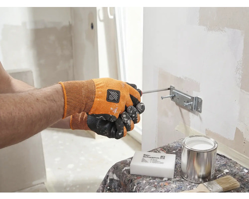 Eine Person befestigt mit einem Schraubenzieher eine Halterung an einer Wand. Auf einem Tisch stehen ein Schwamm, eine Dose und ein Pinsel.