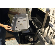 Une femme nettoie le bac de récupération des graisses d'un barbecue.