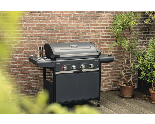 Barbecue à gaz avec quatre brûleurs, table d'appoint et armoire basse devant un mur de briques