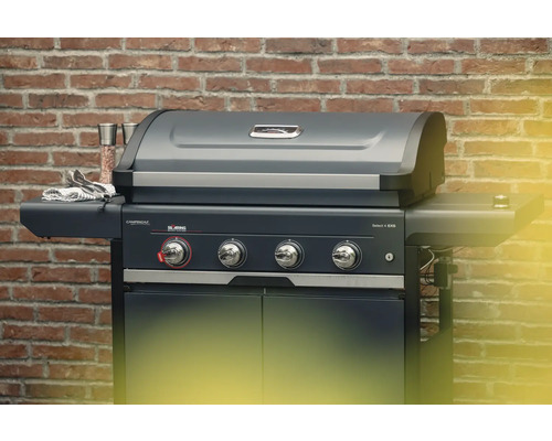 Barbecue à gaz CampinGaz avec quatre brûleurs et brûleur latéral devant un mur de briques