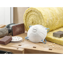 Scène avec masque antipoussière, papier abrasif, ponceuse et laine d'isolation sur un établi.