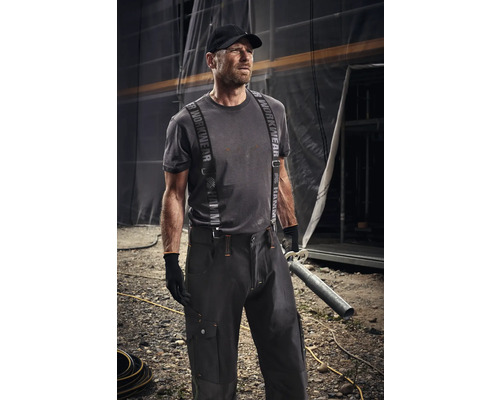 Homme en vêtements de travail avec bretelles et casquette tenant un tuyau