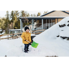 Un enfant avec une pelle à neige dans le jardin enneigé d'une maison