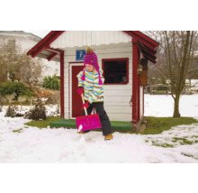 Fille pelletant la neige devant une cabane de jeu dans le jardin