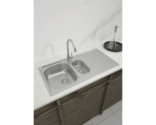 Küchenspüle aus Edelstahl mit Abtropffläche und Wasserhahn auf einer Küchentheke.