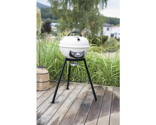 Kugelgrill auf einer Holzterrasse mit Grünpflanzen im Hintergrund.