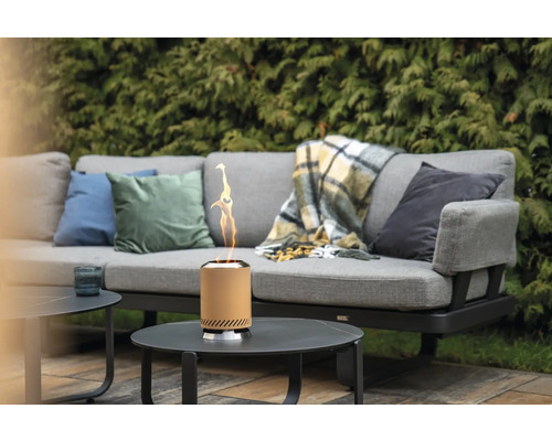 Tischkamin auf einem Gartentisch neben einem grauen Sofa mit Kissen und Decke