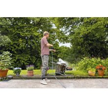 Mann reinigt Schubkarre mit Hochdruckreiniger im Garten.