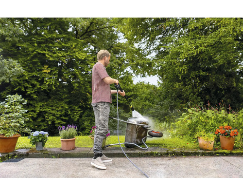 Mann reinigt Schubkarre mit Hochdruckreiniger im Garten.