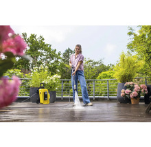 Eine Frau reinigt eine Holzterrasse mit einem Kärcher Hochdruckreiniger K4. Pflanzen und Bäume sind im Hintergrund zu sehen.