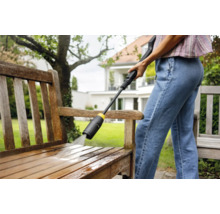 Frau reinigt eine Holzbank mit einem Hochdruckreiniger im Garten.