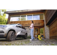 Frau reinigt Auto mit Hochdruckreiniger vor dem Haus