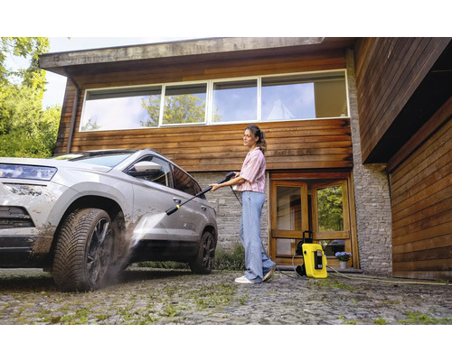 Frau reinigt Auto mit Hochdruckreiniger vor dem Haus