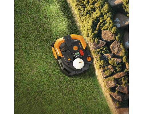 Vue de dessus d'un robot tondeuse à gazon à côté d'un mur de pierre dans le jardin.