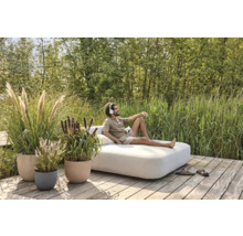 Scène de jardin avec un homme allongé sur un canapé de salon, entouré d'herbes ornementales dans des jardinières.