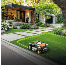 Robot tondeuse à gazon sur pelouse devant maison avec allée pavée