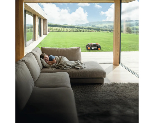 Garçon dort sur un canapé pendant que le robot tondeuse travaille dans le jardin