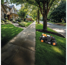 Un robot tondeuse tond la pelouse devant une maison.