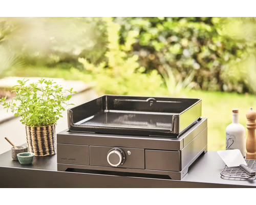 Plancha Forge Adour sur une table avec des ustensiles de cuisine et une plante en arrière-plan