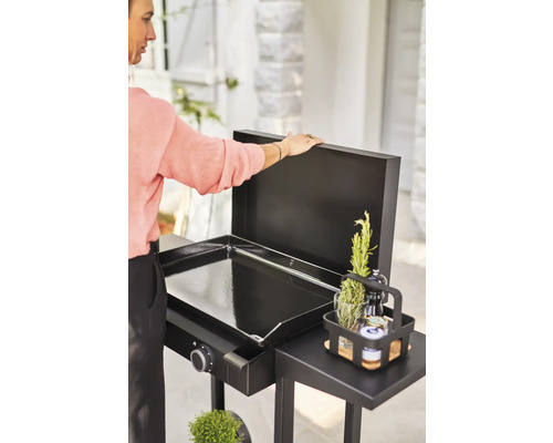 Eine Grillplatte im Aussenbereich mit einem Beistelltisch und einer Person, die den Deckel öffnet.