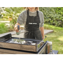 Frau reinigt Grillplatte mit Reinigungsspray und Reinigungsmittel