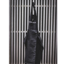 Schwarze Werkstattschürze mit aufgesetzter Tasche und Logo hängt an einer Holzlattenwand.