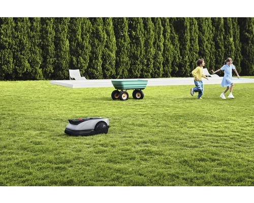 Scène avec robot tondeuse à gazon, brouette et enfants jouant sur une pelouse
