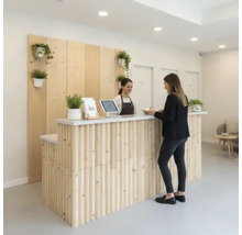 Zone de réception avec comptoir en bois, plantes et deux personnes.